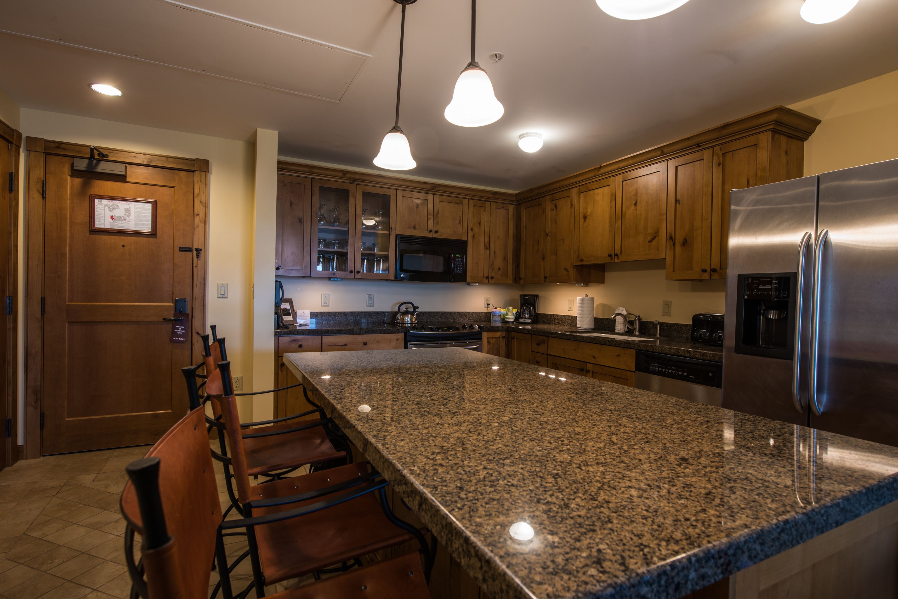 A kitchen with granite countertops, wooden cabinets, stainless steel appliances, and pendant lighting.