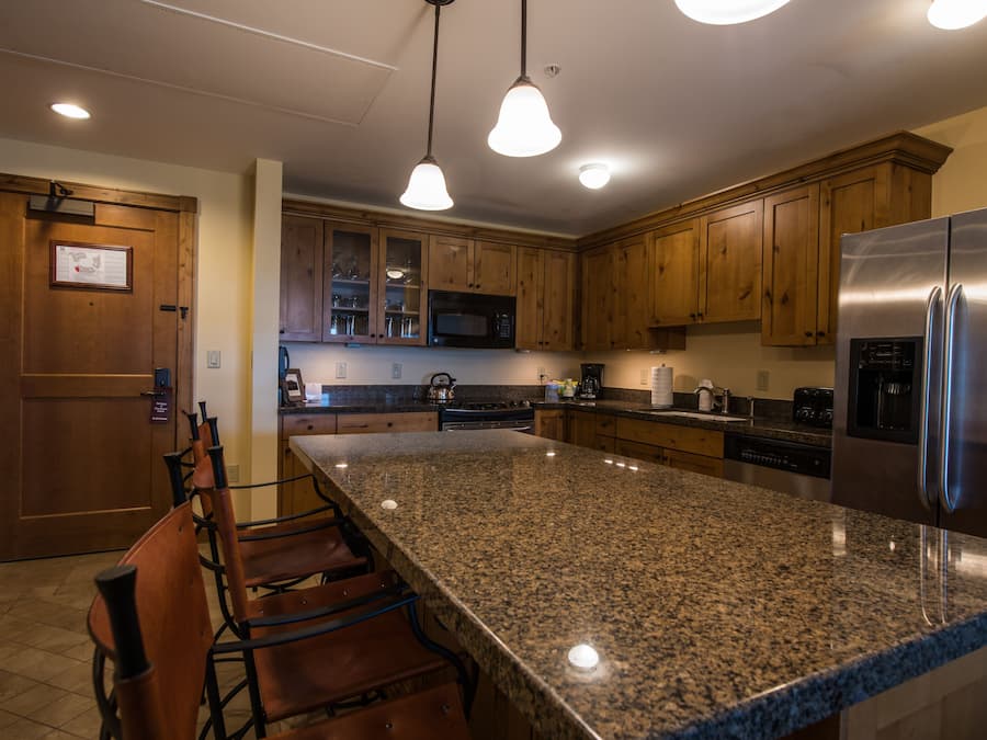 A kitchen with granite countertops, wooden cabinets, stainless steel appliances, and pendant lighting.