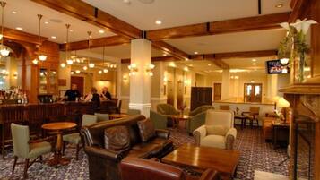 A hotel lobby with wooden beams, leather seating, a bar area, and a television screen.