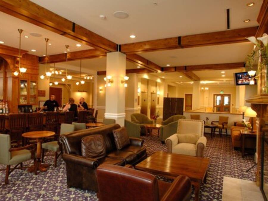A hotel lobby with wooden beams, leather seating, a bar area, and a television screen.