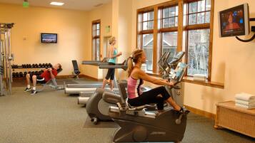 A gym with exercise equipment, a television, and a window with a view of trees.