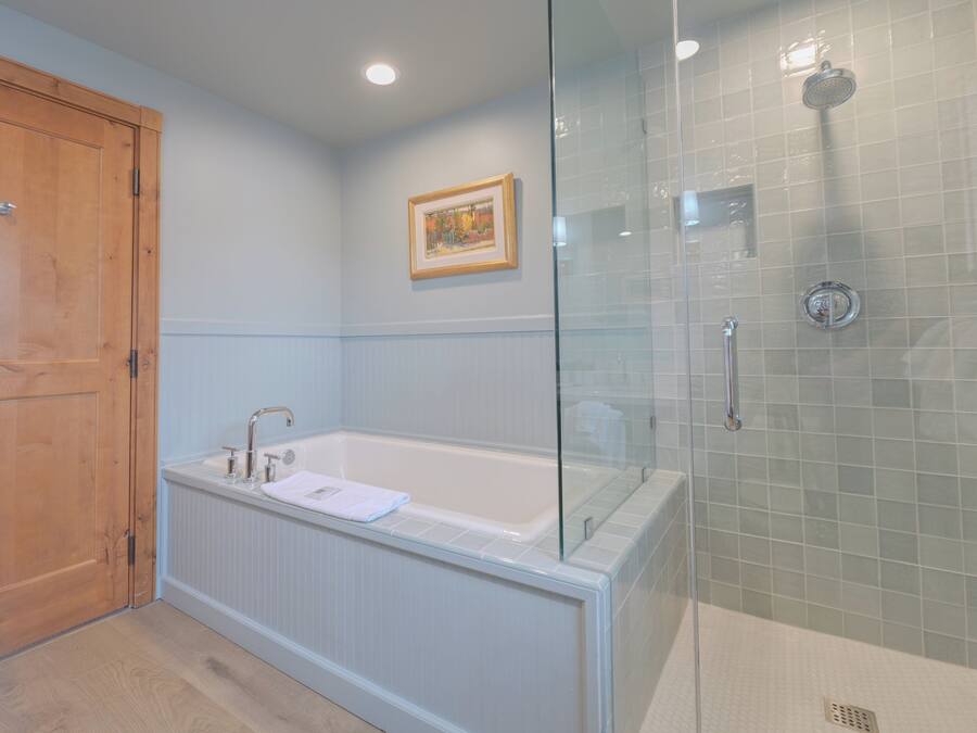 Un baño con ducha envuelta en vidrio, una bañera blanca y una puerta de madera.