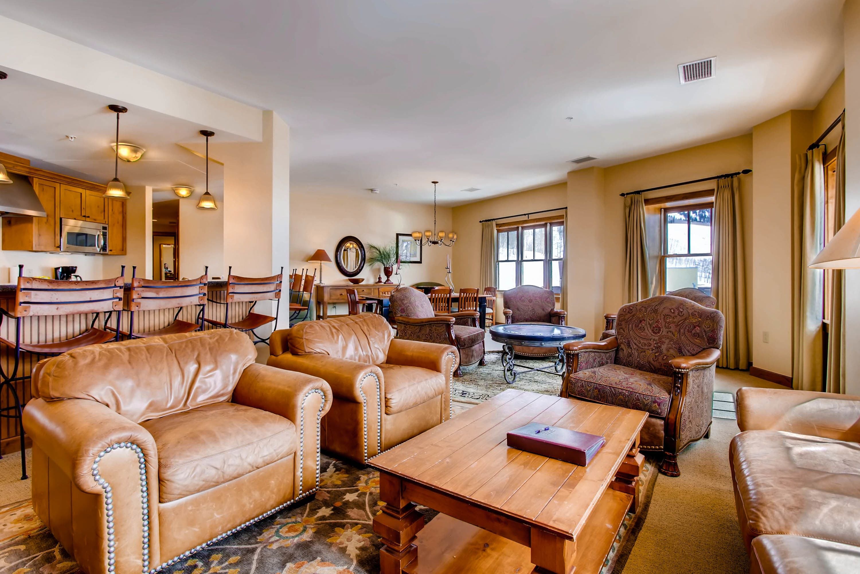 A spacious living room with leather sofas, a wooden coffee table, and a dining area with wooden chairs and a chandelier.