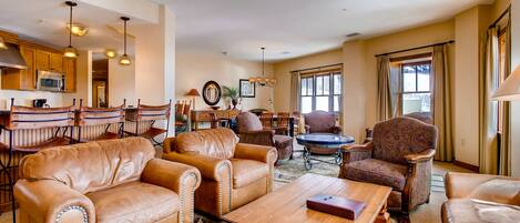 A spacious living room with leather sofas, a wooden coffee table, and a dining area with wooden chairs and a chandelier.