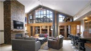 A spacious living area with a stone fireplace, large windows, and a high ceiling. - The Lodge at Mountaineer Square, A Vail Resorts Property (Crested Butte)
