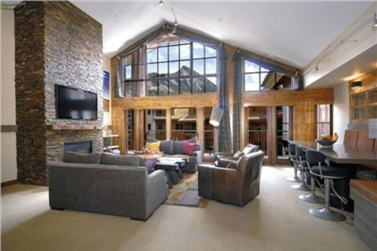 A spacious living area with a stone fireplace, large windows, and a high ceiling.