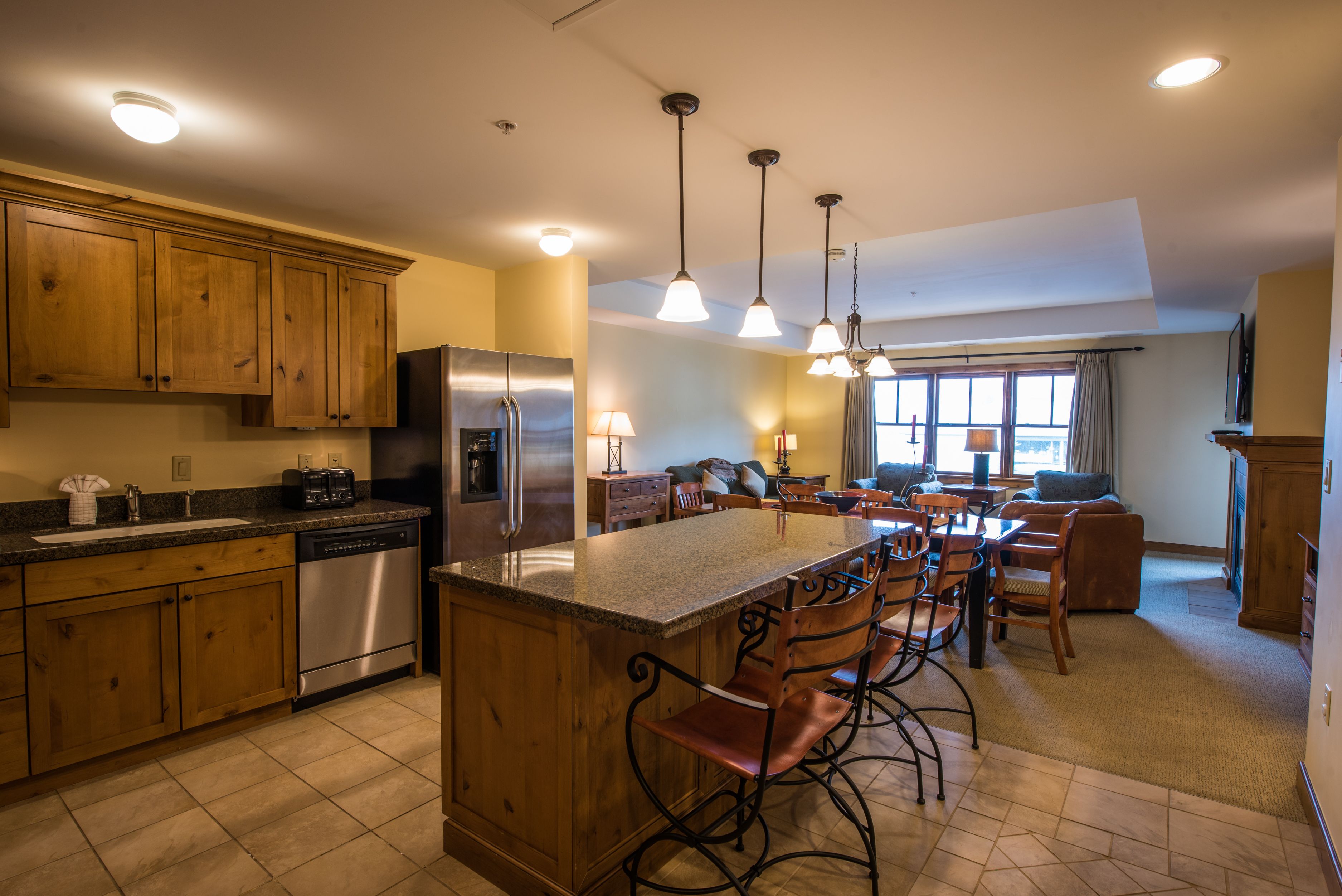 A kitchen with wooden cabinets, stainless steel appliances, a central island with bar stools, and pendant lighting.