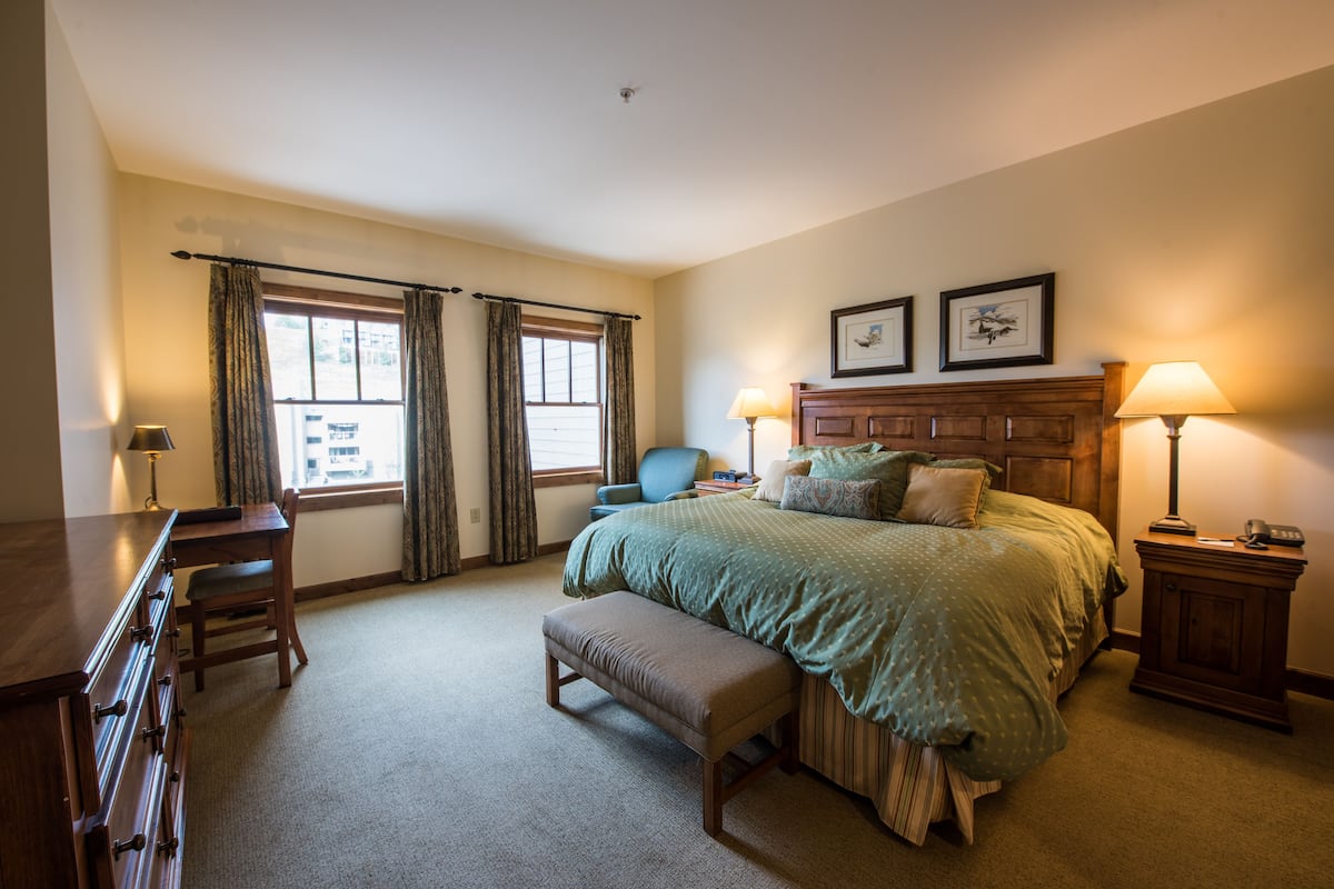A bedroom with a bed, bedside lamps, a desk, and a chair.