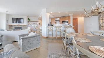 Un salon moderne avec une cheminée, un coin repas avec une grande table en bois et une cuisine dotée de meubles en bois et d’un four à micro-ondes encastré.