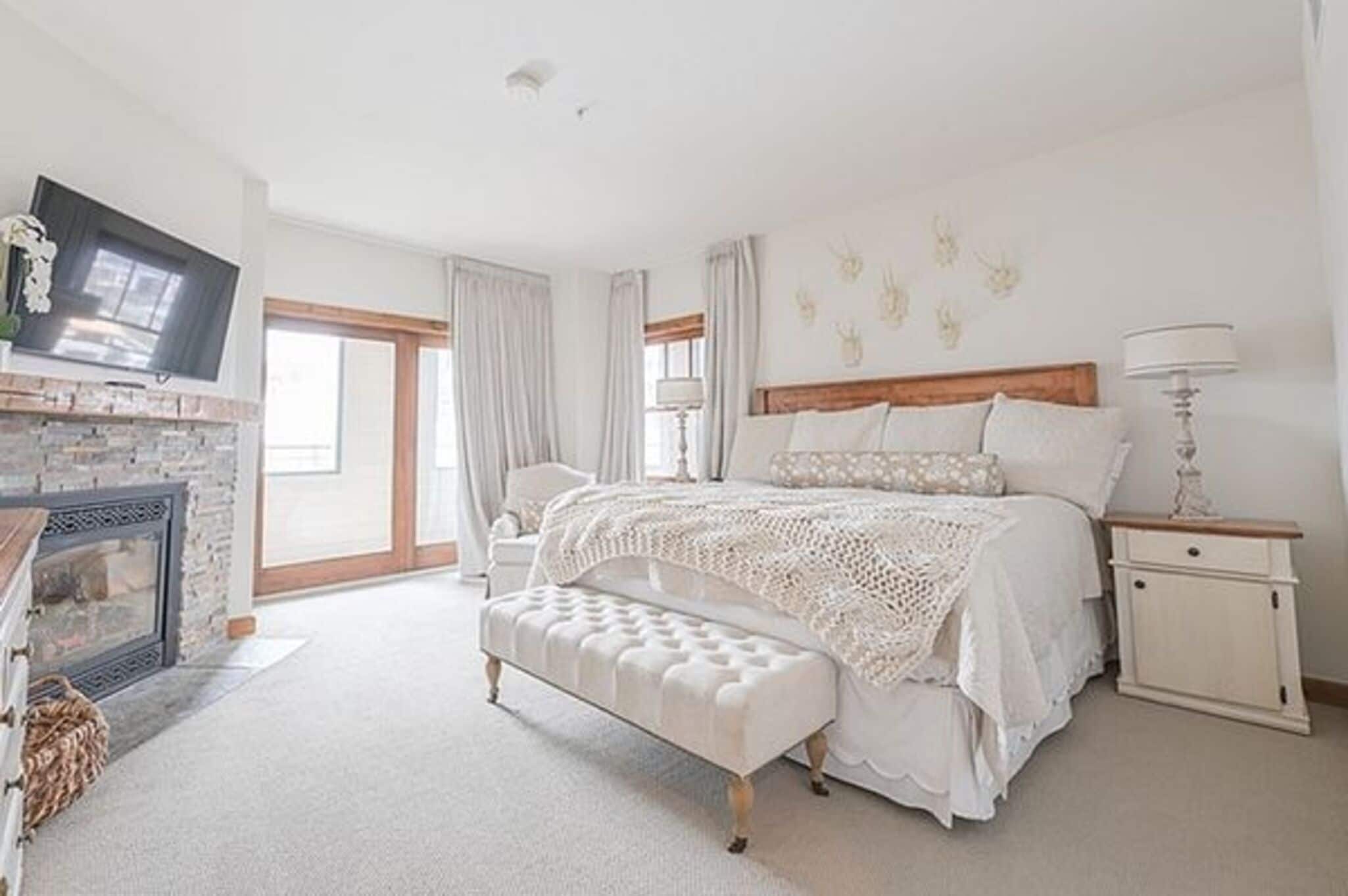 Een slaapkamer met een groot bed, een bankje, een nachtkastje, een lamp, een open haard en een televisie.