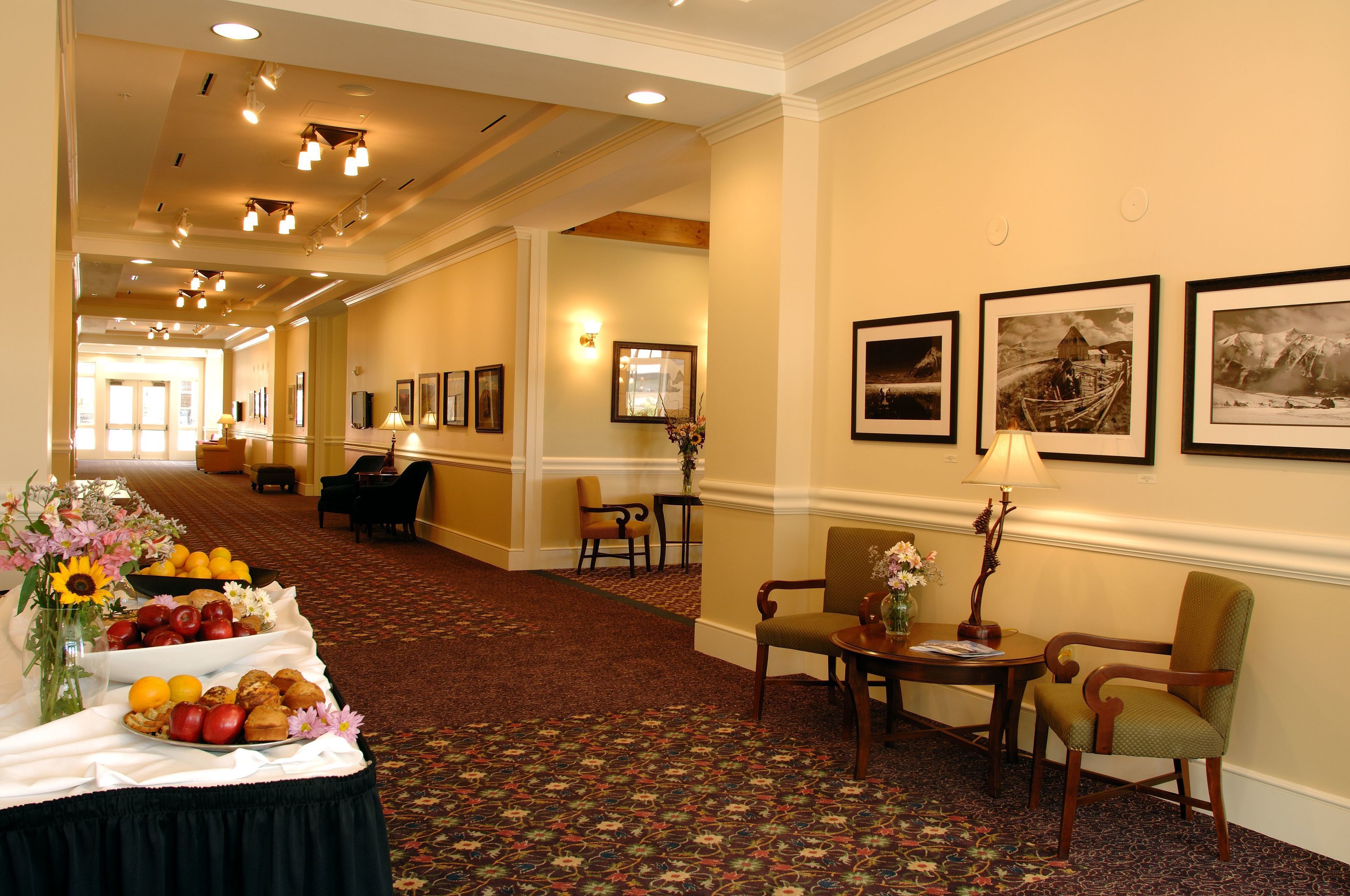 A hotel lobby with a reception desk, seating area, and a buffet table with fruits and pastries.
