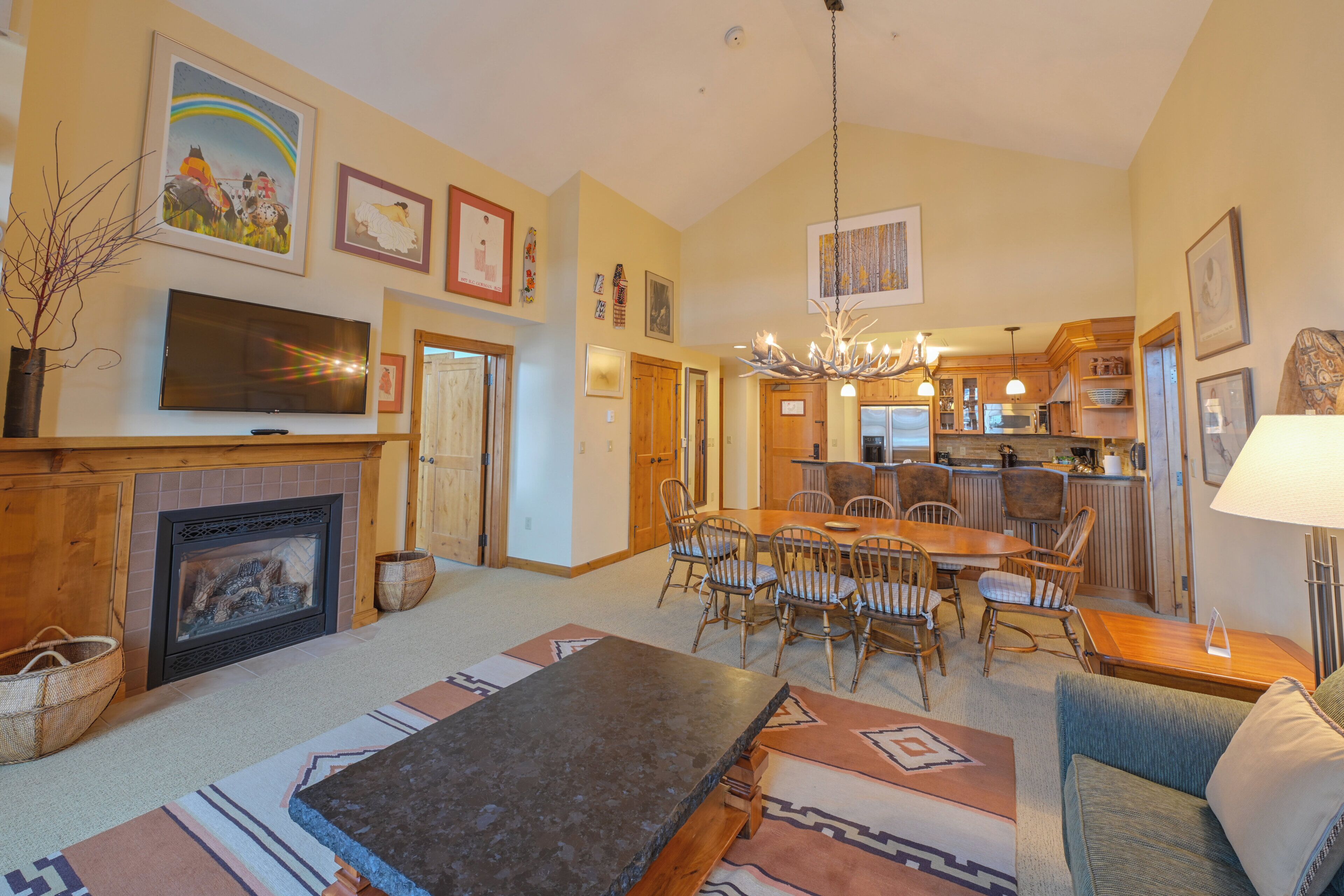 A spacious living room with a fireplace, a dining area, and a kitchen in the background.