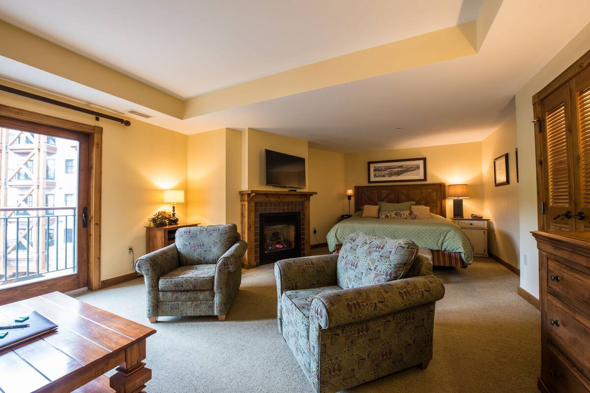A cozy bedroom with a fireplace, two armchairs, a bed, and a wooden dresser.