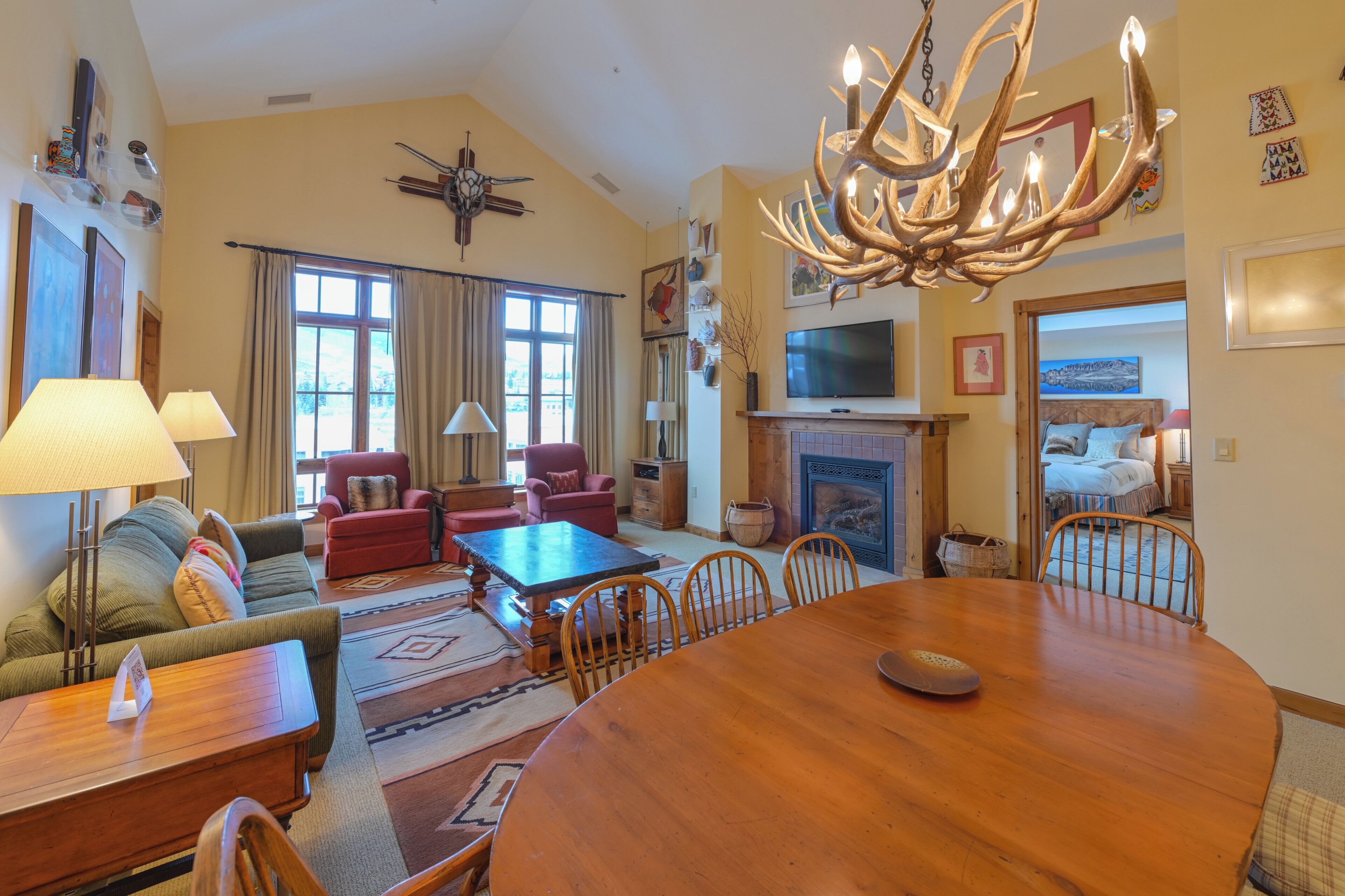 A spacious living room with a large wooden dining table, comfortable seating, a fireplace, and a television.