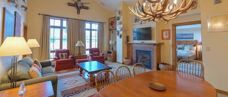 A spacious living room with a large wooden dining table, comfortable seating, a fireplace, and a television.