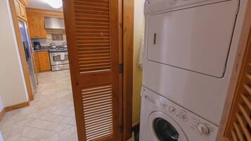A laundry room with stacked washers and dryers, wooden cabinets, and a tiled floor.