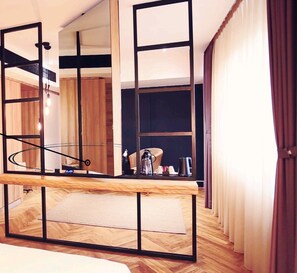 A modern hotel room with a wooden floor, a large mirror, and a wooden desk.