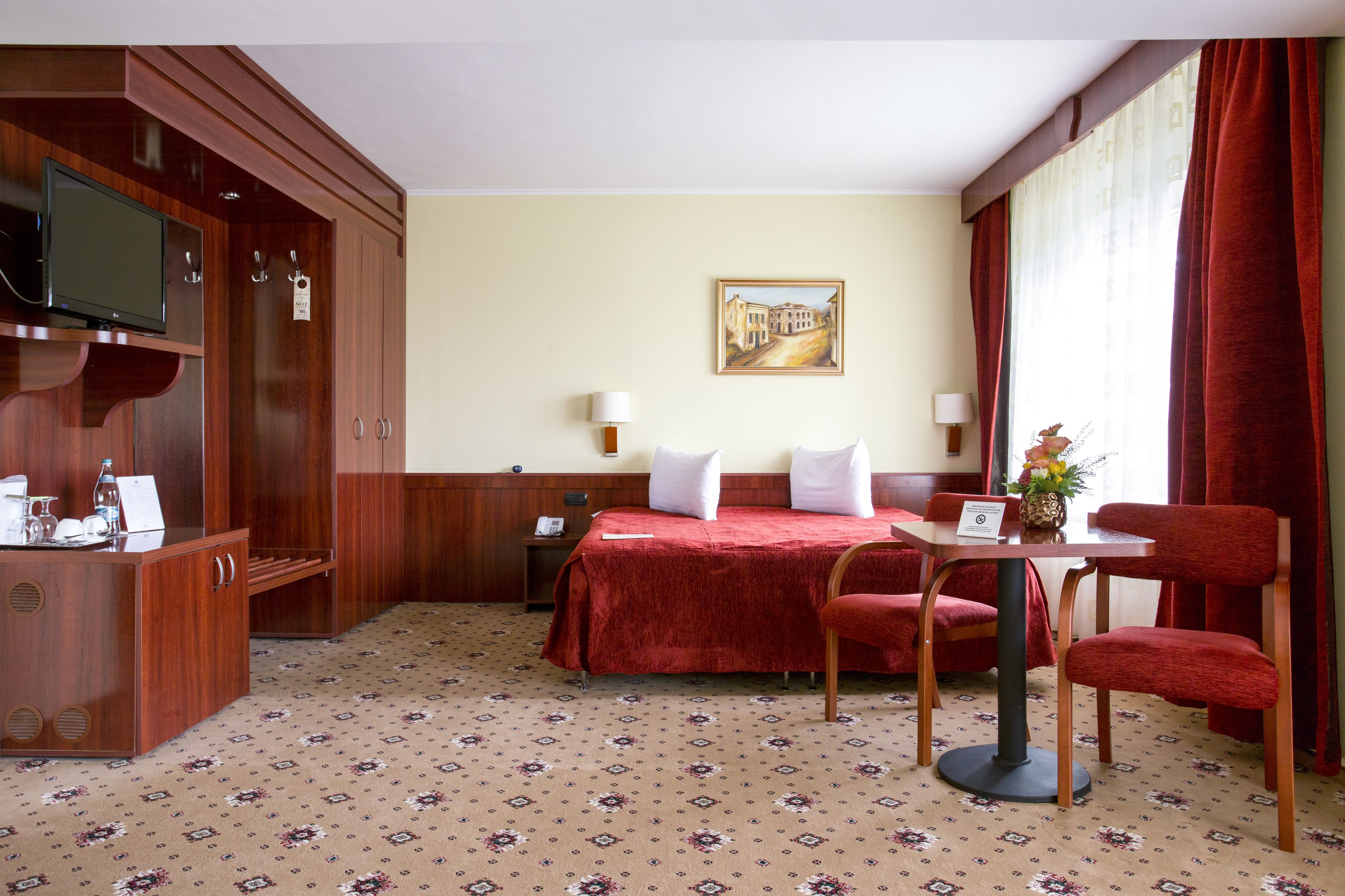 A hotel room with a bed, a desk with a chair, a television, and a painting on the wall.