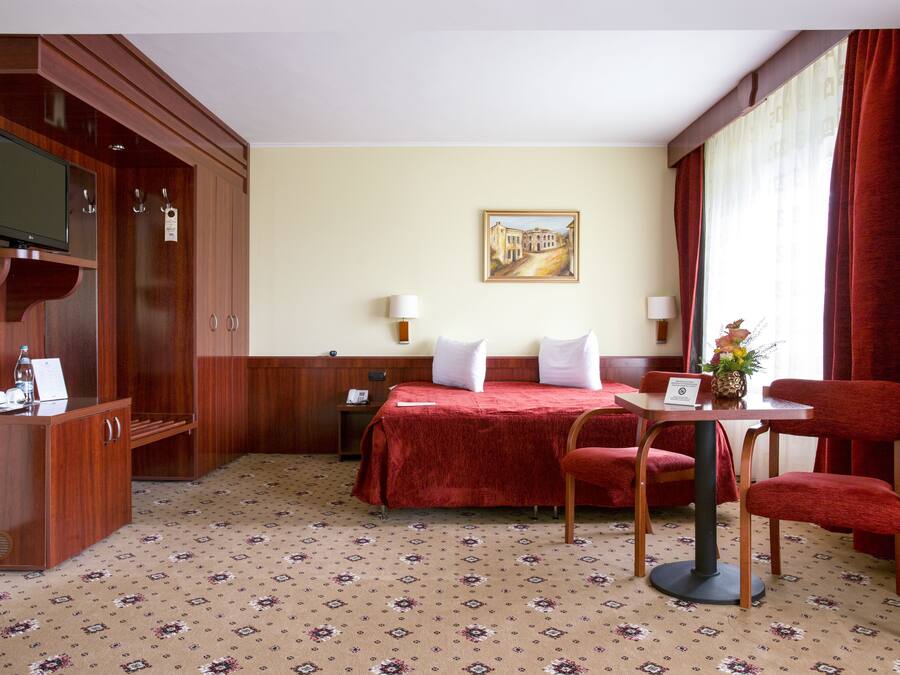 Habitación de hotel con cama, escritorio, silla, televisor y un cuadro en la pared.