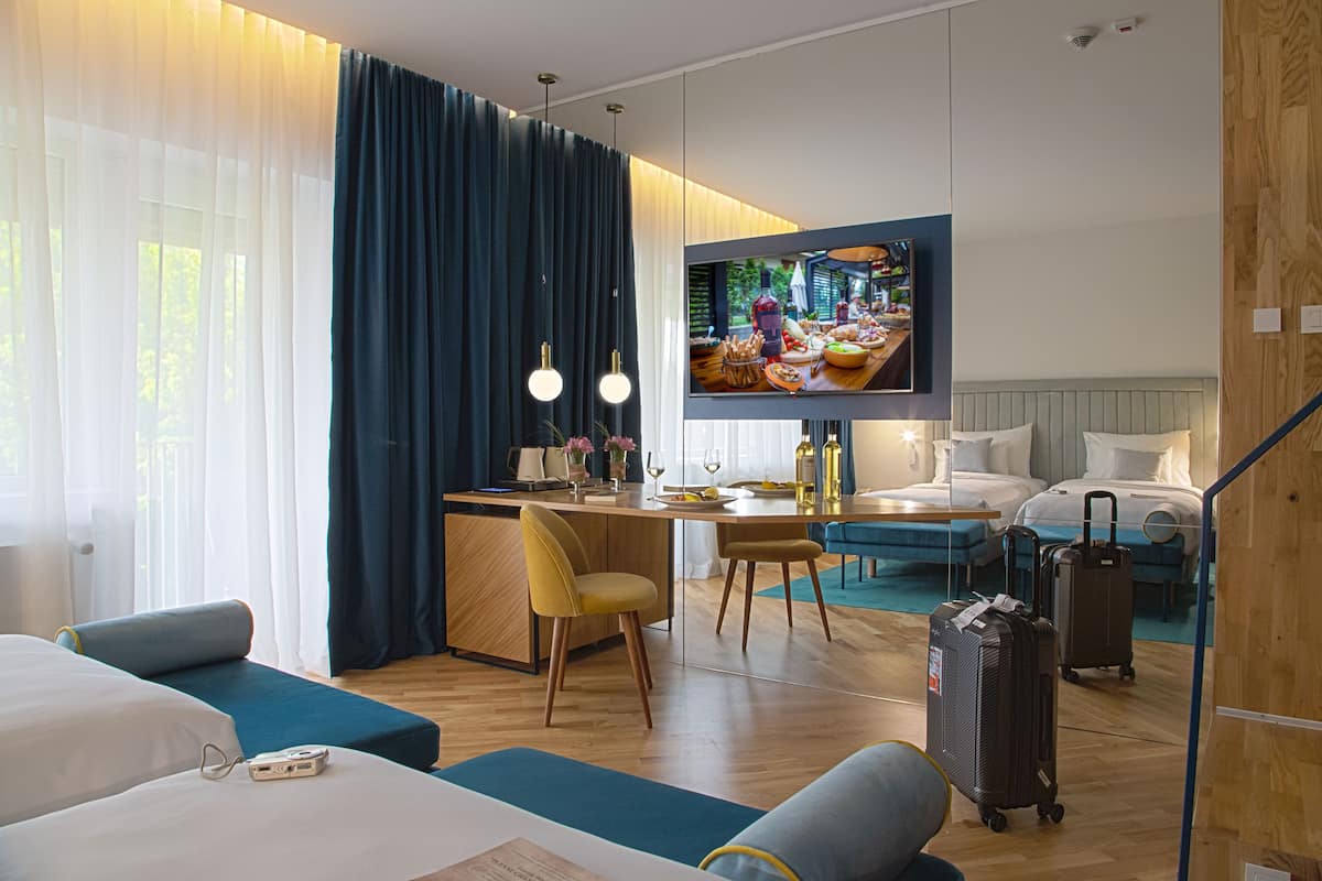 Habitación de hotel con una cama, un escritorio con silla, un televisor y una maleta.