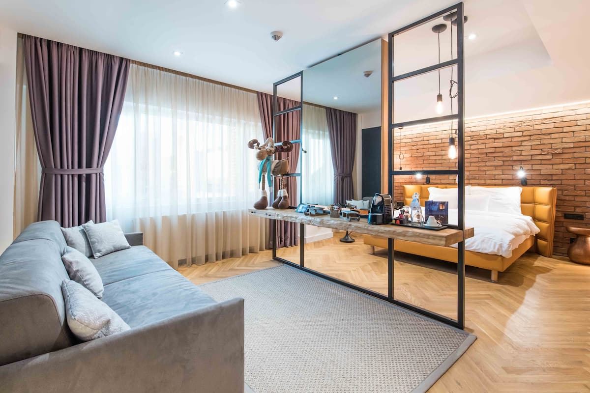 Una habitación de hotel moderna con sofá, cama, un espejo grande y piso de madera.