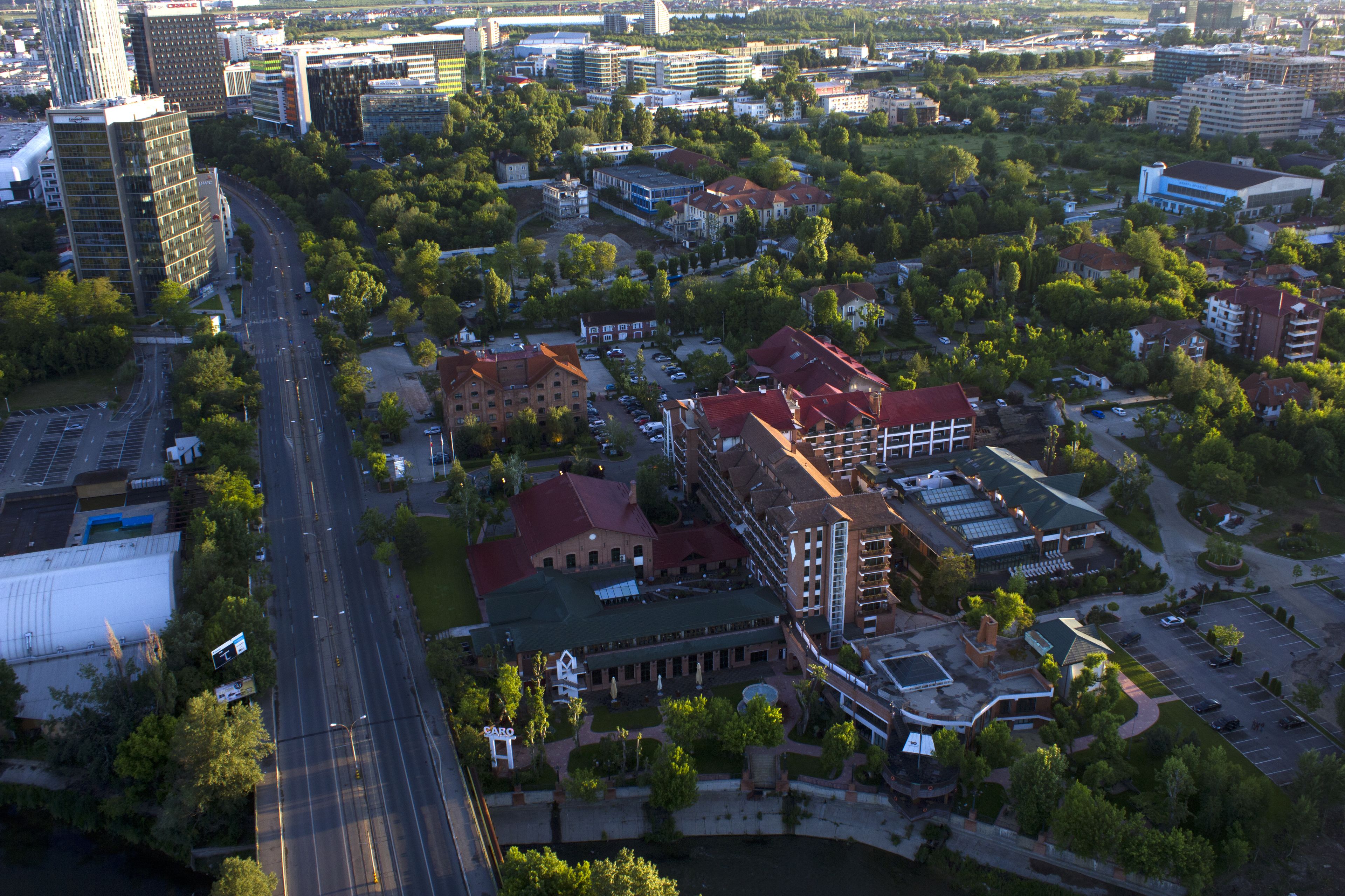 An aerial view of a cityscape with a mix of modern and traditional buildings, a central road, and surrounding greenery.