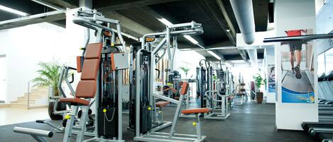 A gym with various exercise machines, a treadmill, and a large mirror.