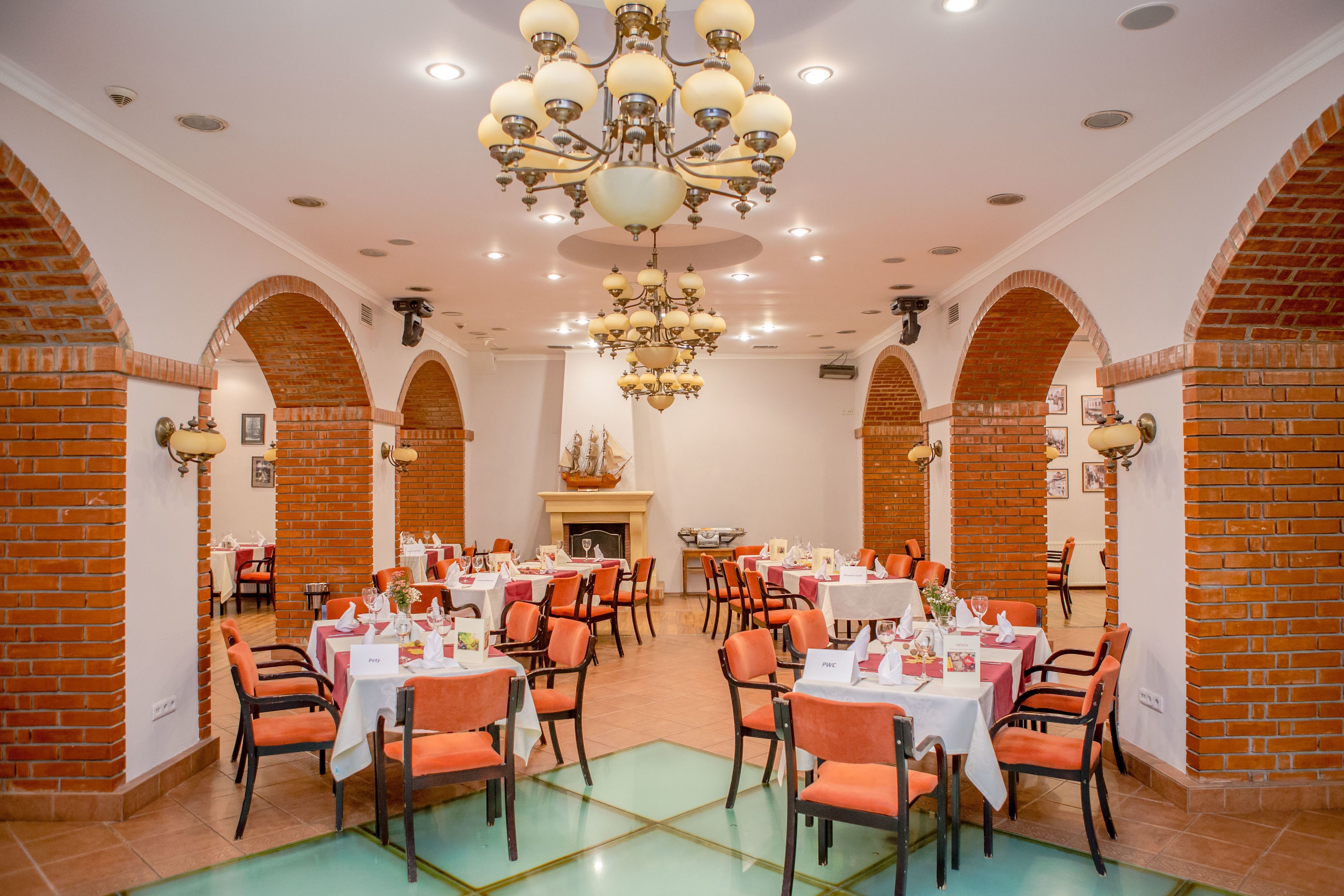 A spacious dining area with brick arches, white tables, and orange chairs.
