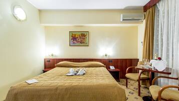 Une chambre d’hôtel avec un lit, un bureau avec un téléphone, une chaise et une table avec une bouteille et des verres.