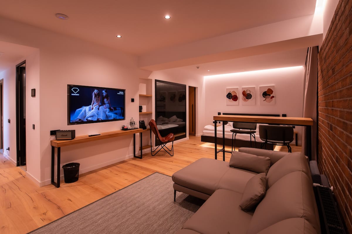 Una sala moderna con un televisor de pantalla plana grande, un sofá, un comedor con mesa y sillas, y una pared de ladrillo.