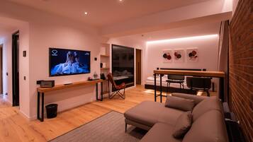 Una sala moderna con un televisor de pantalla plana grande, un sofá, un comedor con mesa y sillas, y una pared de ladrillo.
