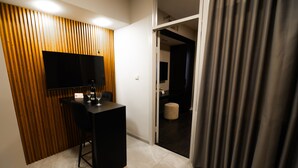 A modern room with a flat-screen TV mounted on a wooden panel wall, a small black table with a bottle and glasses, and a door leading to another room. - Lev Yerushalayim (Jerusalem)