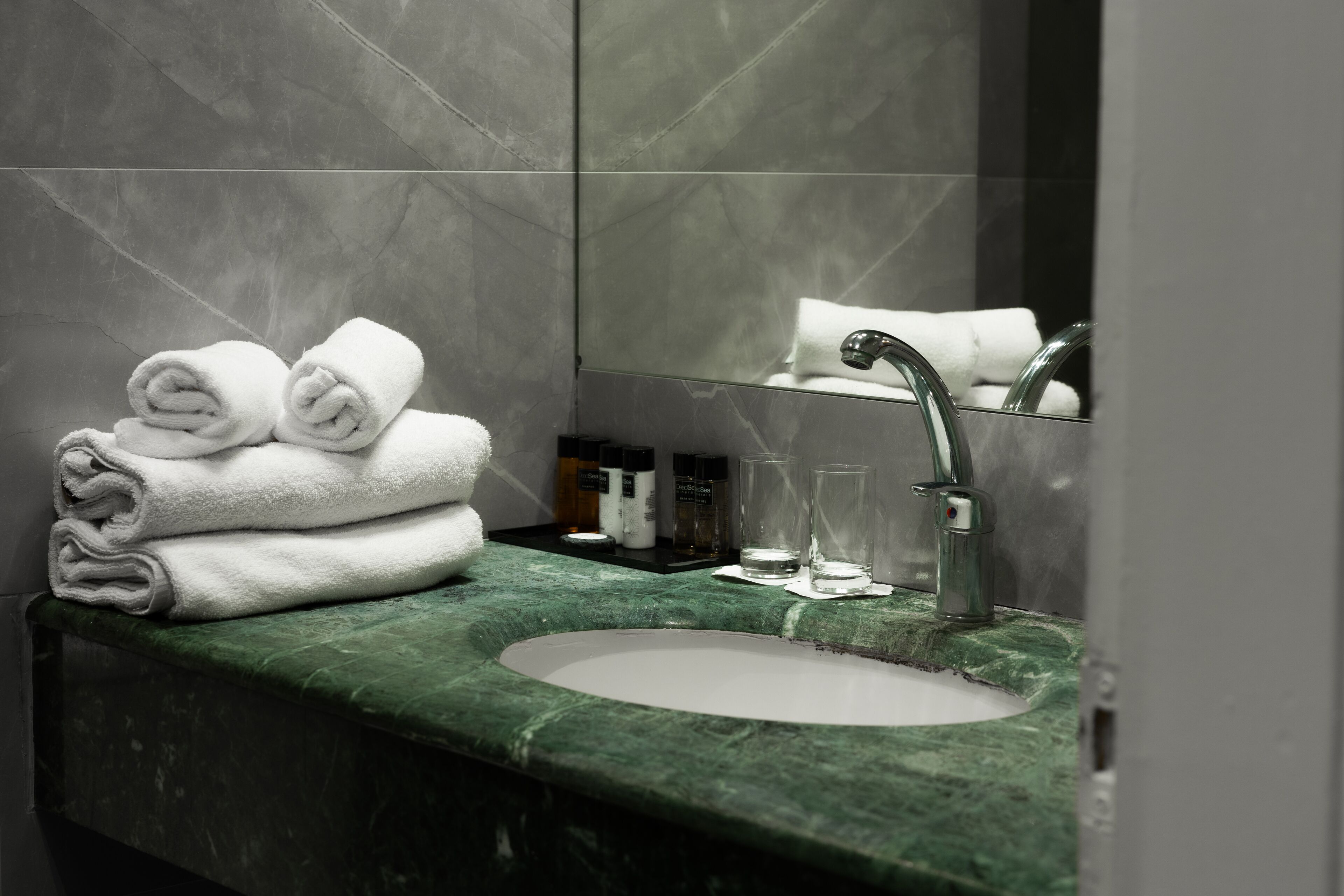 A bathroom with a green marble sink, a mirror, and neatly folded white towels on the counter.