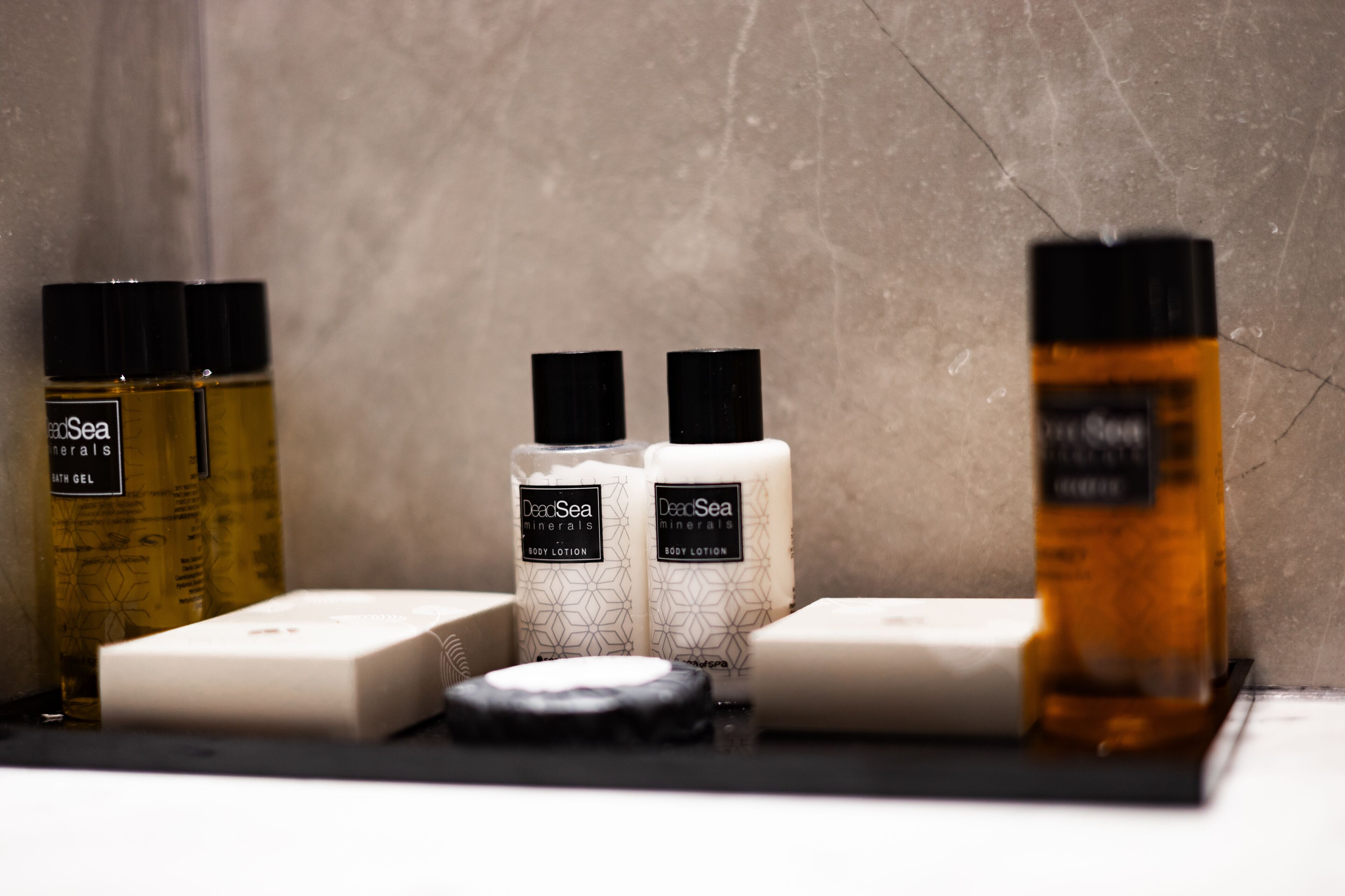 Un estante de baño con diversos artículos de aseo, incluyendo botellas de loción corporal, una pastilla de jabón y un frasco de gel de baño.