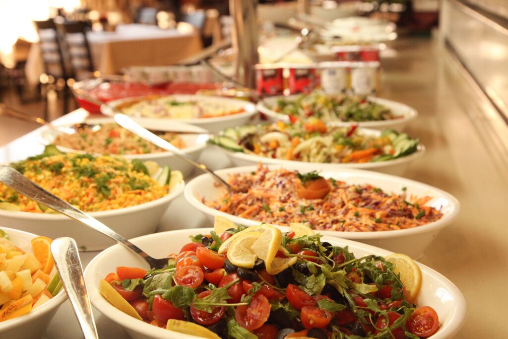Un bufé con diversos platos, entre ellos ensaladas, pasta y arroz.
