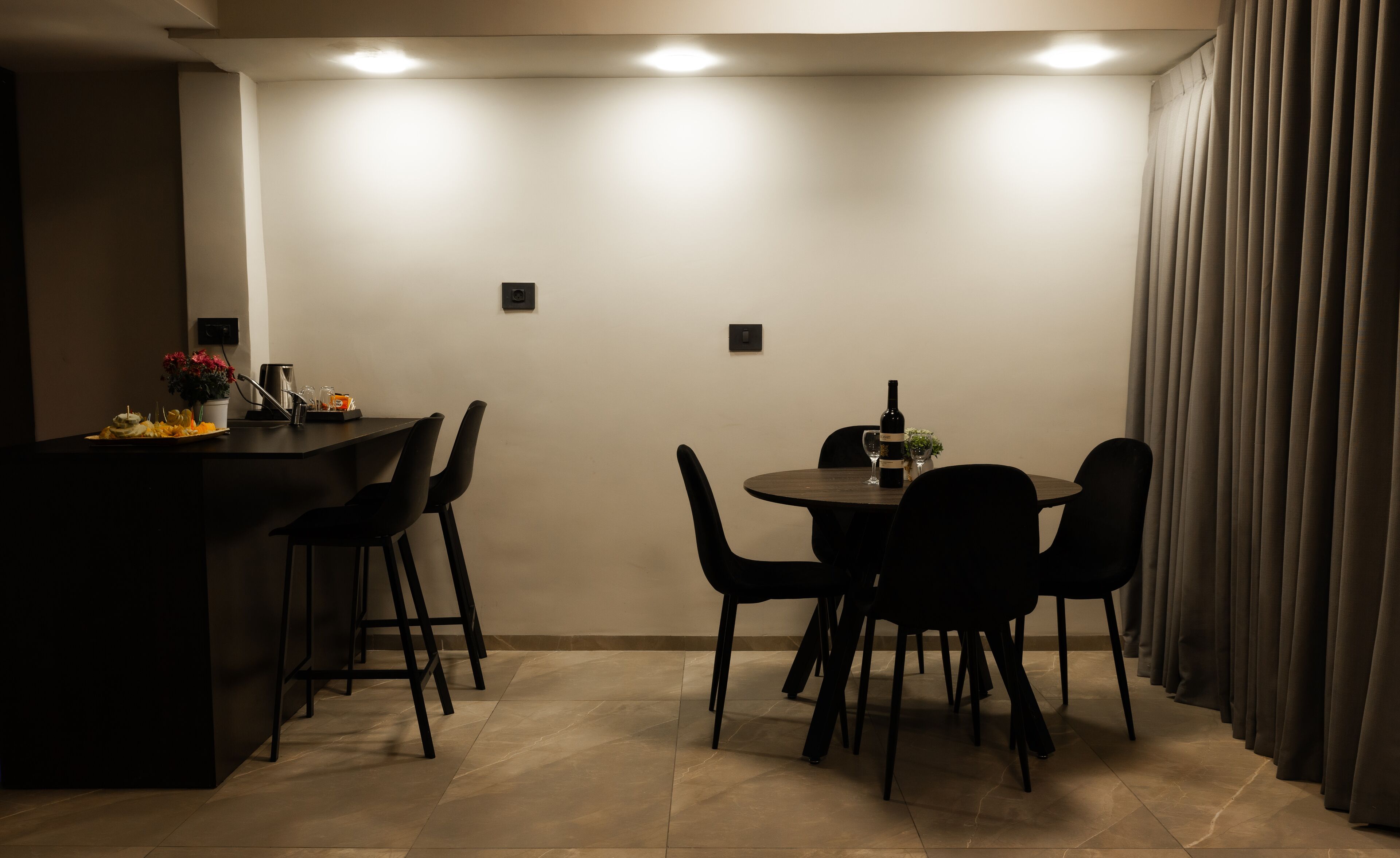 A dining area with a bar, a round table with chairs, and a curtain on the right.