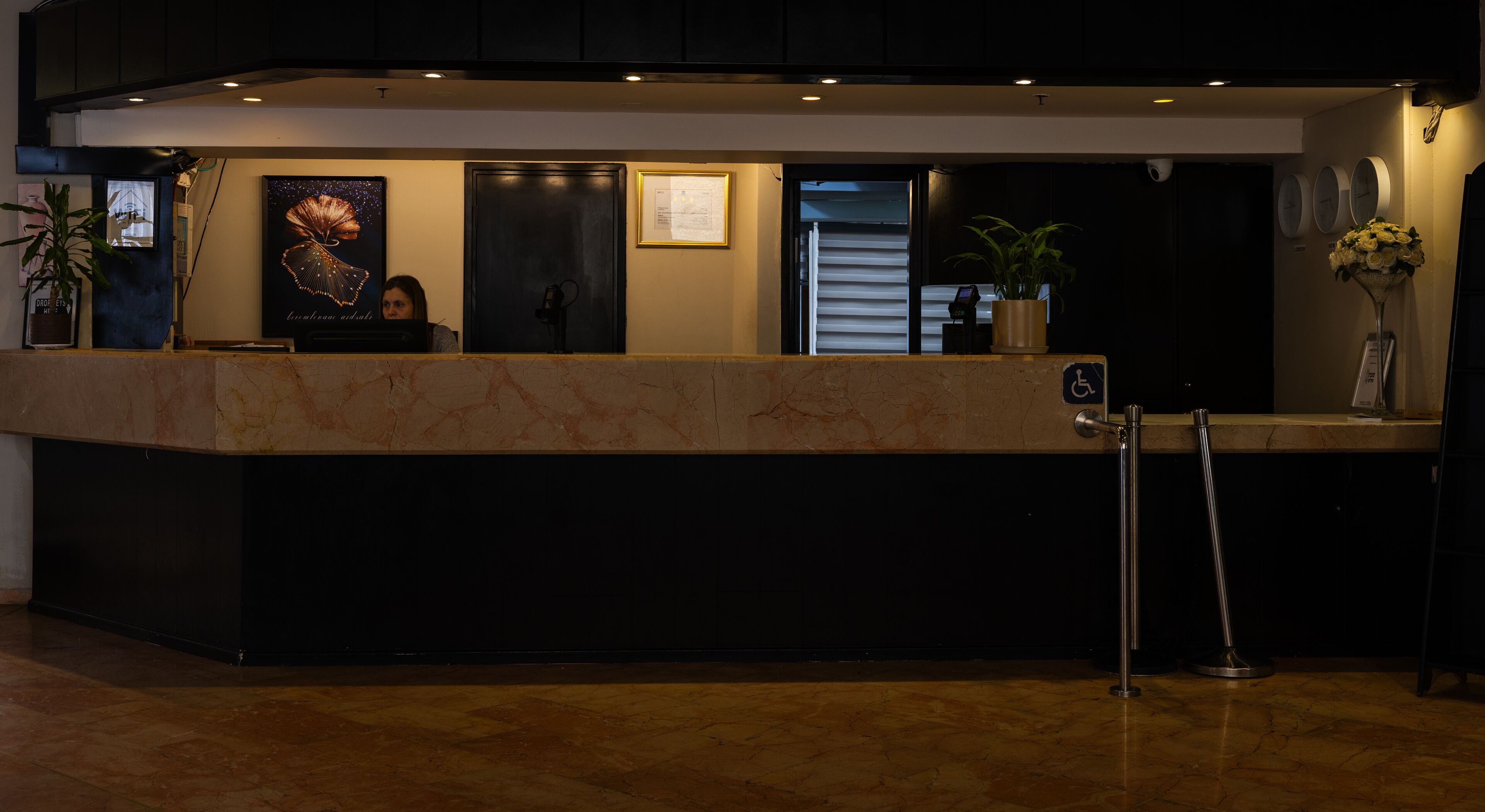 A reception desk with a marble counter, a wheelchair accessibility sign, and a potted plant.