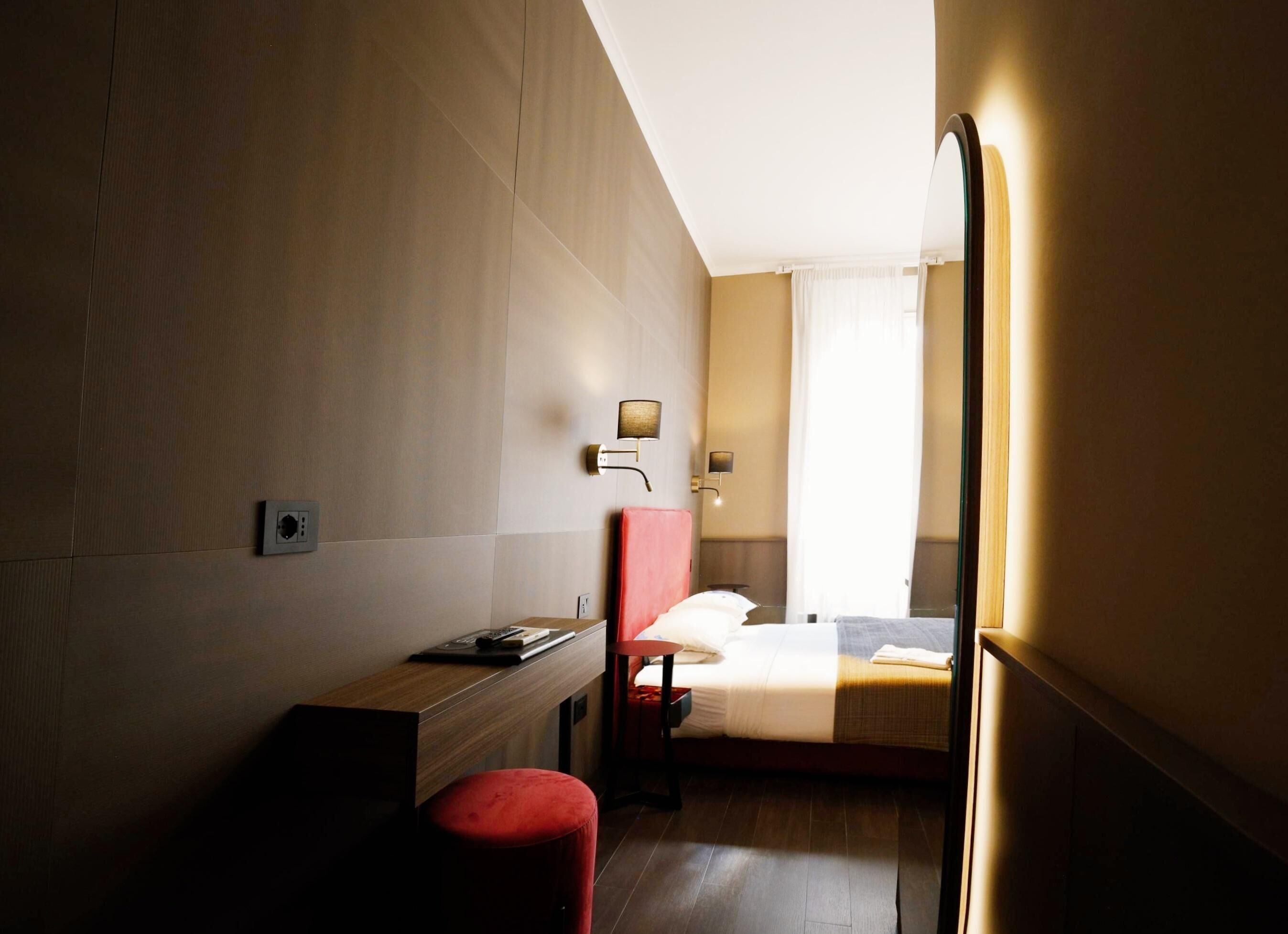 A hotel room with a bed, a desk, a chair, and a mirror.