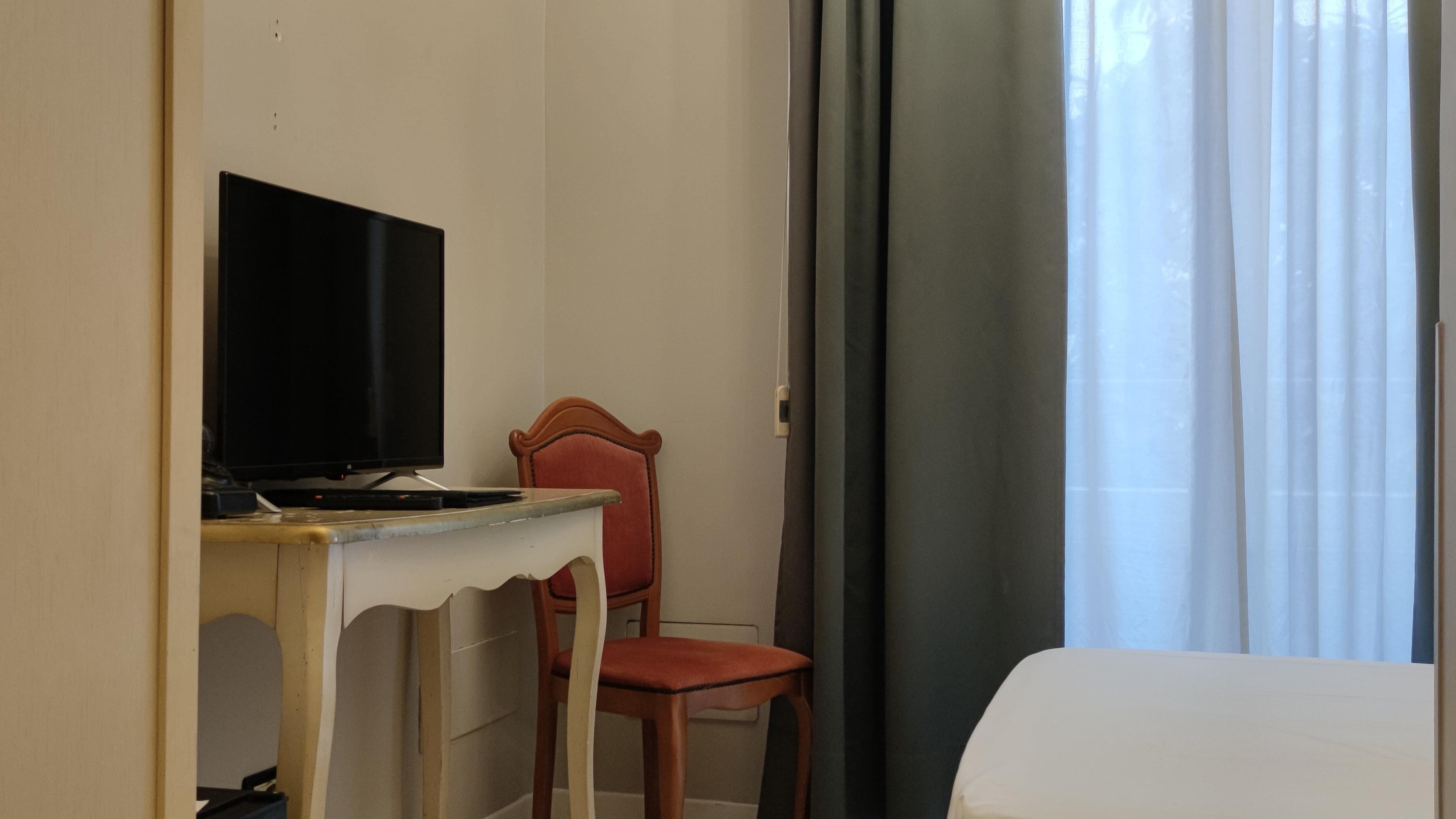 Una camera d'albergo con una scrivania, una televisione, una sedia e un letto.