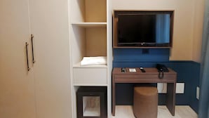 A hotel room with a wardrobe, a desk with a television, a telephone, and a small stool.