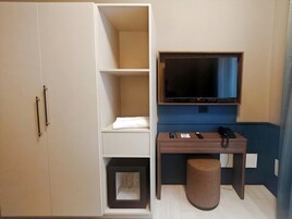 Habitación de hotel con armario, escritorio, televisor, teléfono y un pequeño taburete.
