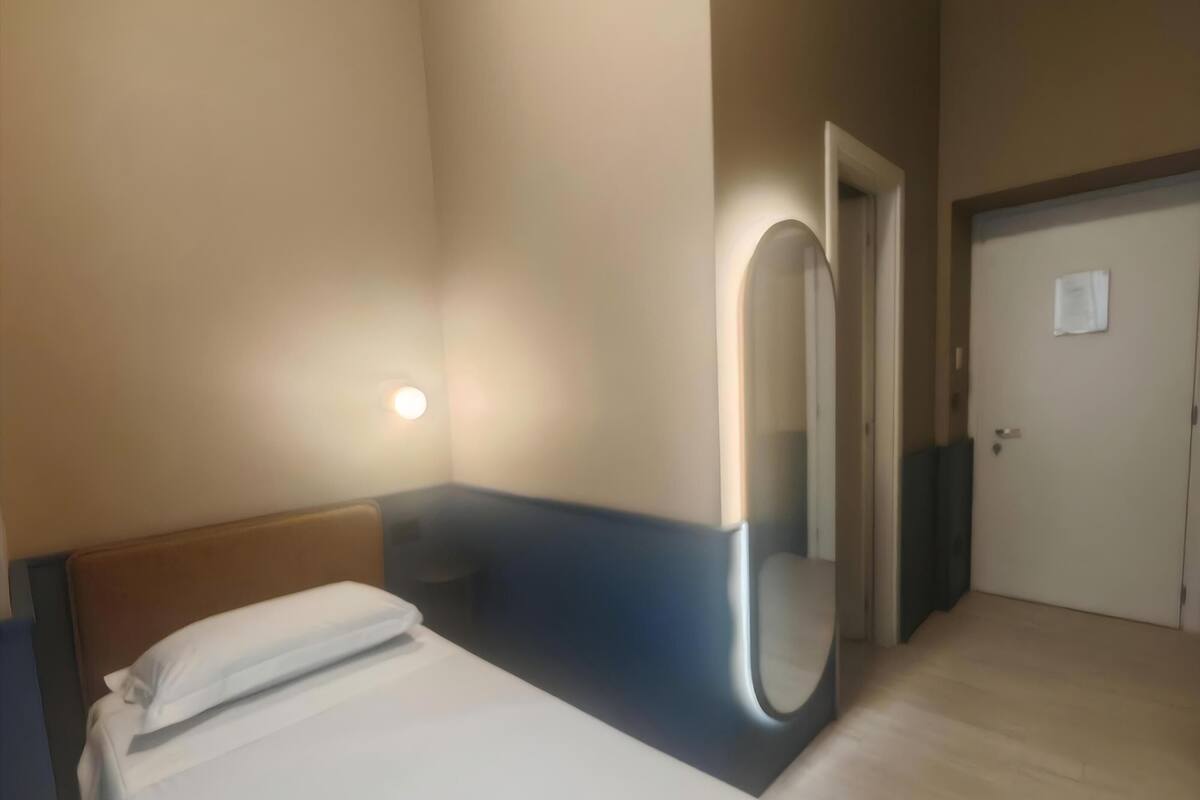 A hotel room with a bed, a bedside table, a mirror, and a door.
