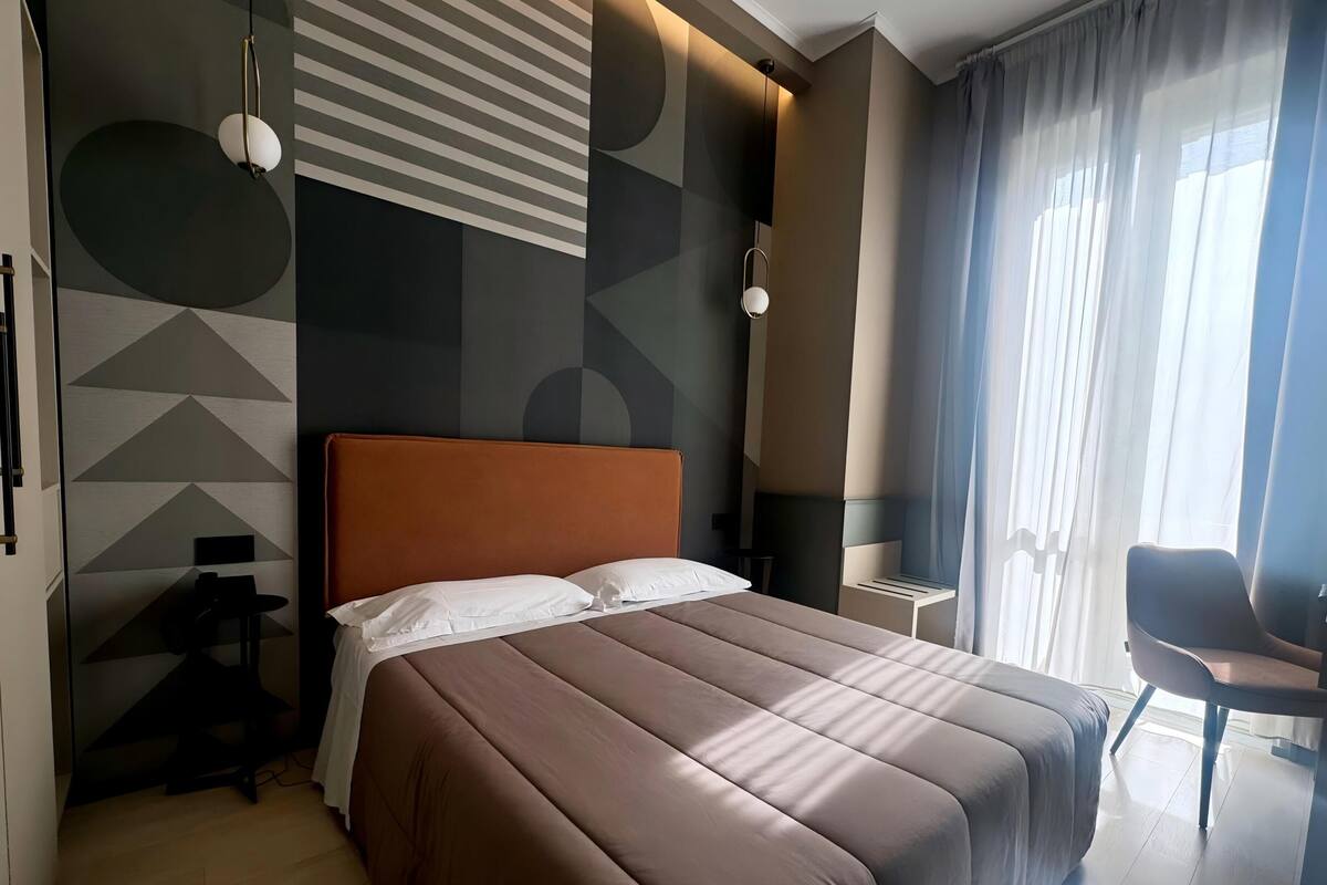 A modern hotel room with a large bed, a chair, and a desk.