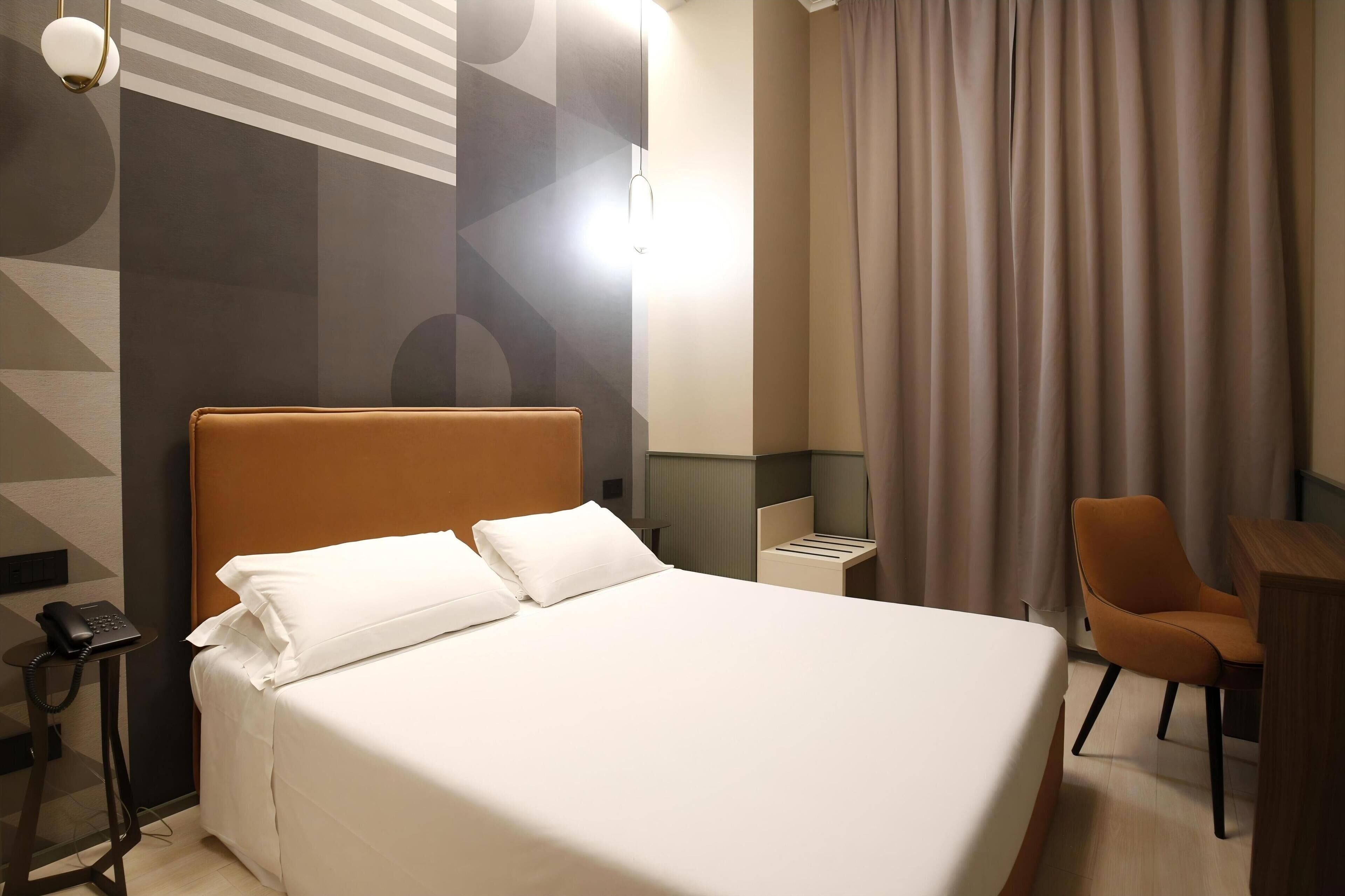 A hotel room with a large bed, a desk, a chair, a phone, and a curtain.