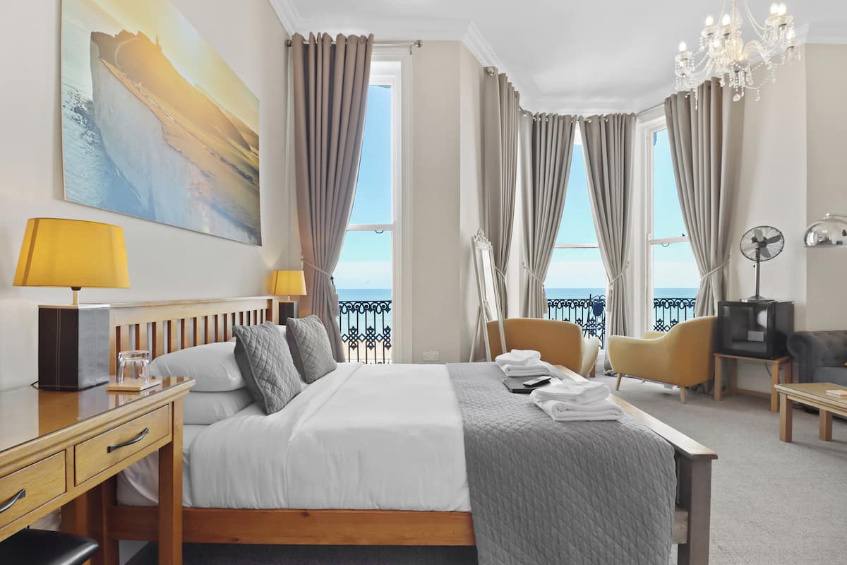 A hotel room with a bed, bedside tables, a desk, a chair, a TV, and a balcony with curtains.