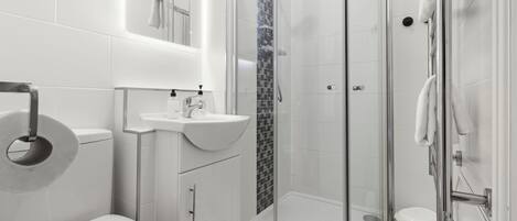 A modern bathroom with a toilet, sink, shower, and glass-enclosed shower stall.