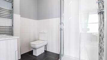 A modern bathroom with a toilet, a shower with a glass door, and a white sink.