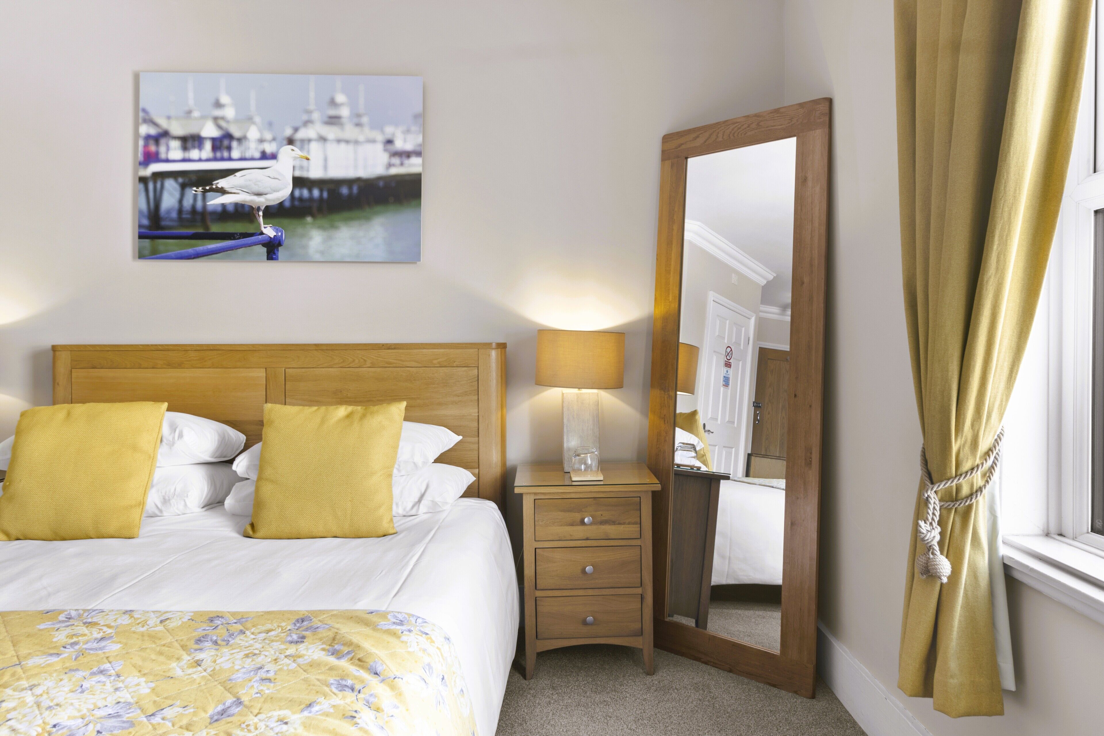 A hotel room with a bed, a nightstand with a lamp, a mirror, and a window with curtains.