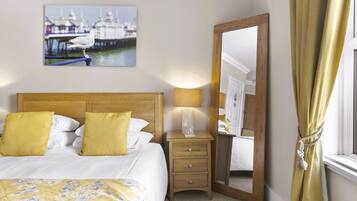 A hotel room with a bed, a nightstand with a lamp, a mirror, and a window with curtains.