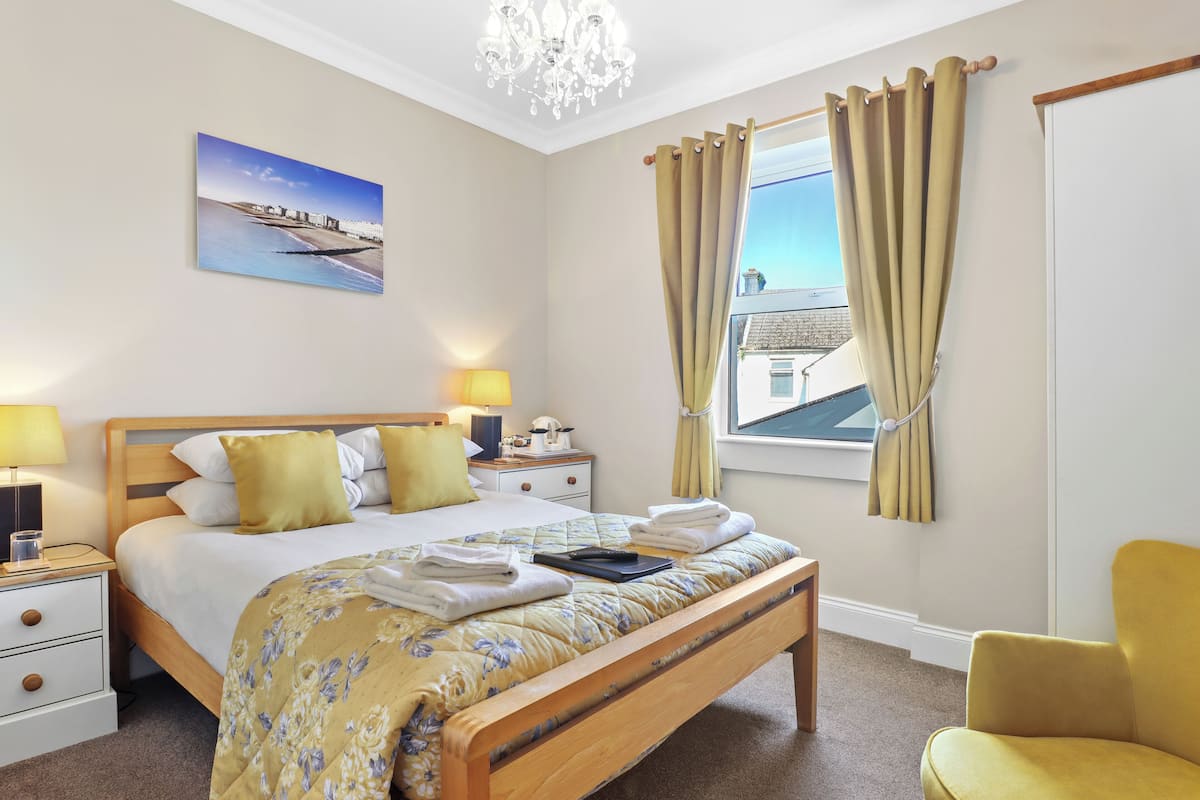 A neatly arranged bedroom with a bed, bedside tables, a chair, and a window with curtains.